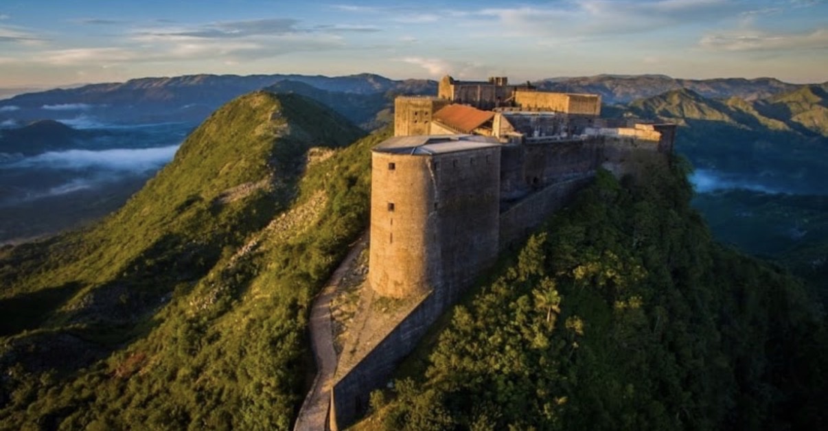 Aerial view of the Citadelle Laferrière fortress on a green mountain peak at golden hour, Haiti